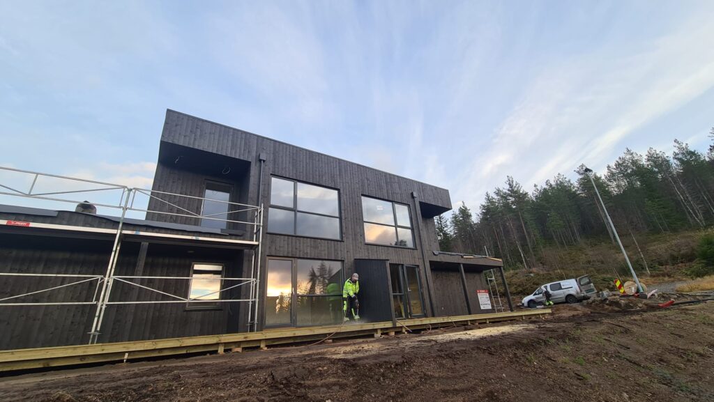 Ubehandlet svart trehus under bygging i naturområde med arbeidere og utstyr rundt, moderne arkitektur, miljøvennlig byggemateriale, bygningsarbeid, igangsetting, bygging av nytt hus.